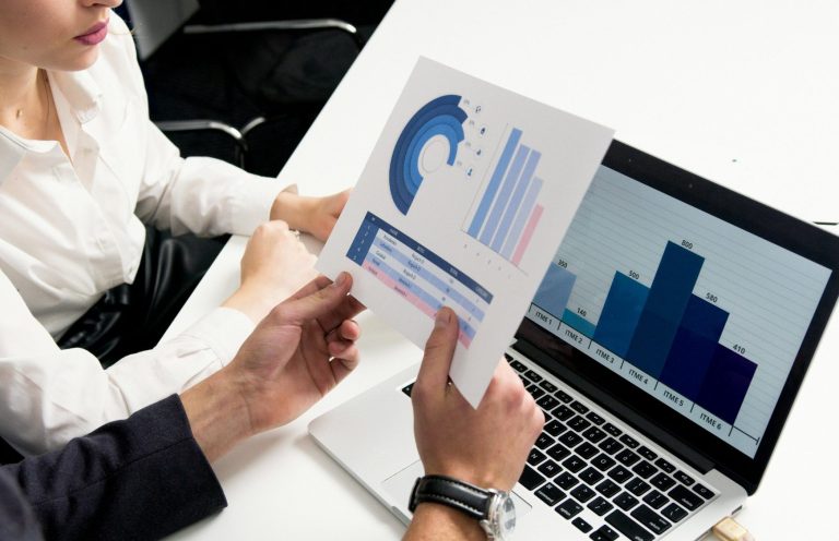 Makroaufnahme von Diagrammen auf einem Blatt und einem Laptop mit Grafiken.