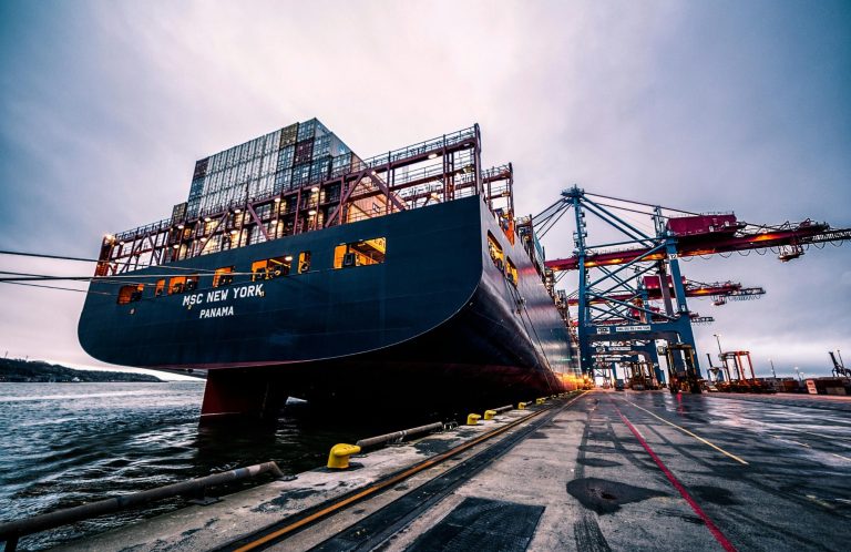 Containerschiff an einer Hafenanlage, umgeben von Kräne und Wasser.