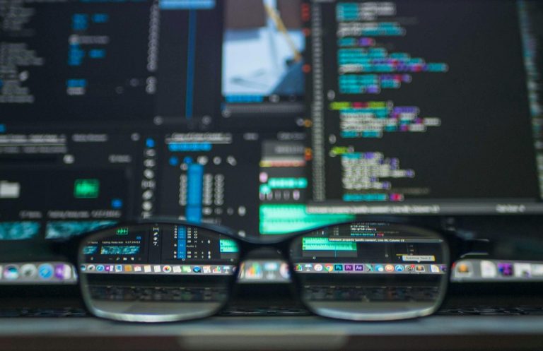Eine Brille liegt vor einem Laptop mit Code und technischen Grafiken auf dem Bildschirm.
